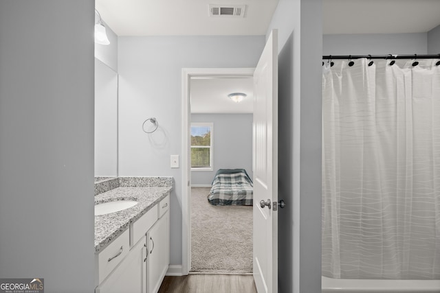 ensuite bathroom featuring connected bathroom, vanity, visible vents, baseboards, and wood finished floors