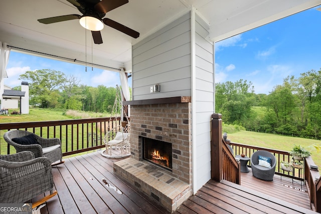 deck featuring a lawn, a ceiling fan, and an outdoor brick fireplace