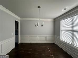 3421 Andover Way, Buford, GA 30519 - unfurnished dining area featuring dark wood-style flooring, a notable chandelier, a wainscoted wall, visible vents, and ornamental molding