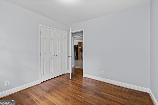 unfurnished bedroom with freestanding refrigerator, baseboards, wood finished floors, and a closet