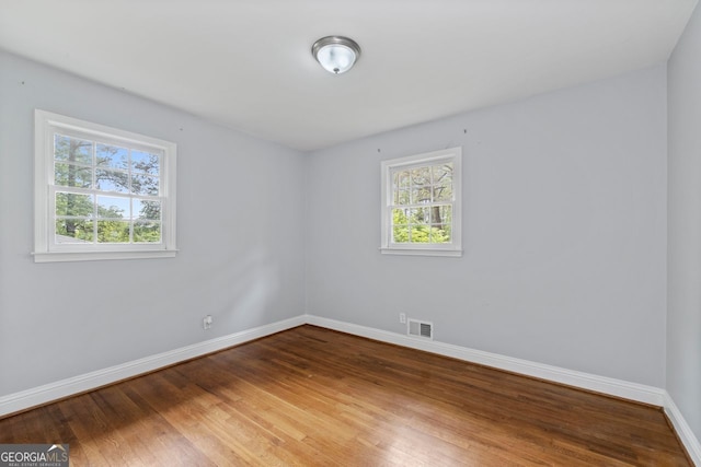 unfurnished room with baseboards, wood finished floors, and visible vents