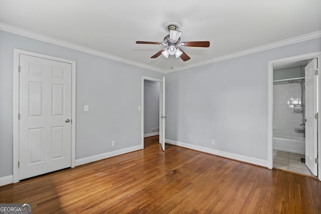 unfurnished bedroom with crown molding, ensuite bath, wood-type flooring, a ceiling fan, and baseboards