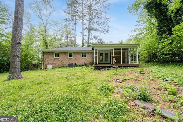 rear view of house featuring a sunroom, a lawn, brick siding, and cooling unit