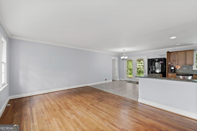 unfurnished living room with crown molding, baseboards, an inviting chandelier, and light wood-style flooring