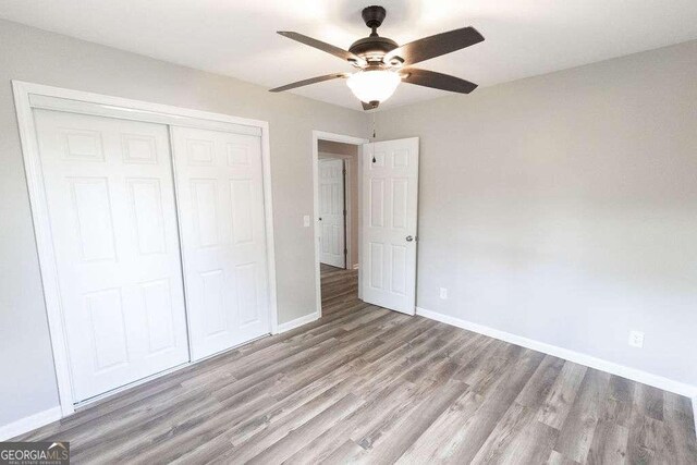 unfurnished bedroom with a closet, a ceiling fan, wood finished floors, and baseboards