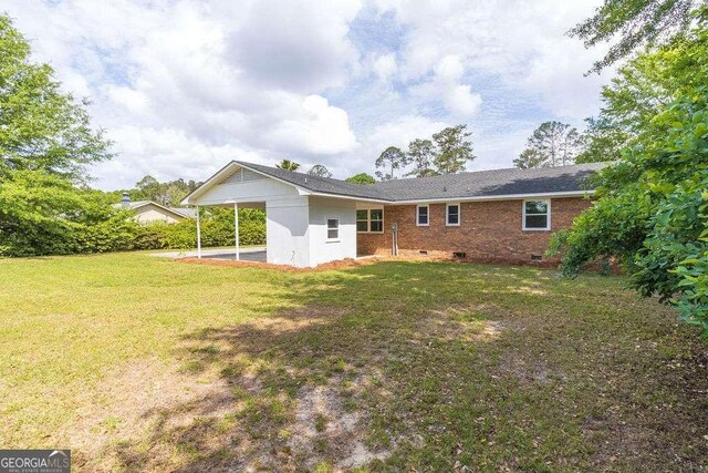 back of house featuring a lawn, a carport, and crawl space