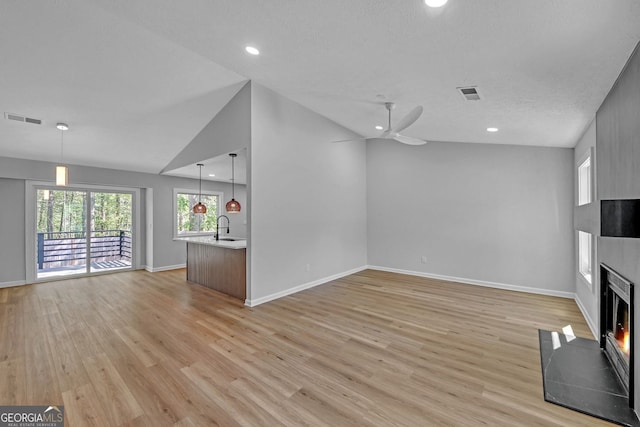 unfurnished living room featuring a sink, a large fireplace, light wood finished floors, and visible vents