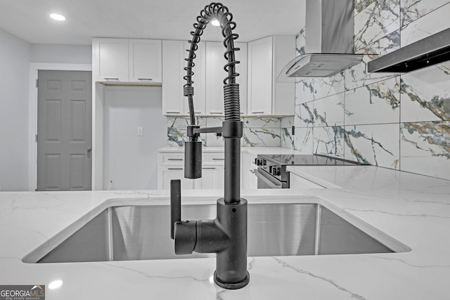 details featuring light stone countertops, wall chimney range hood, stainless steel electric range, white cabinets, and tasteful backsplash