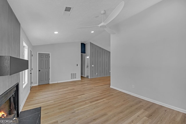 unfurnished living room featuring baseboards, light wood-type flooring, a large fireplace, a ceiling fan, and vaulted ceiling