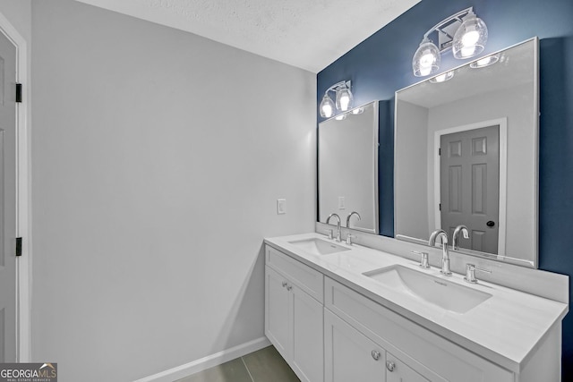 full bathroom featuring baseboards, a sink, a textured ceiling, and double vanity