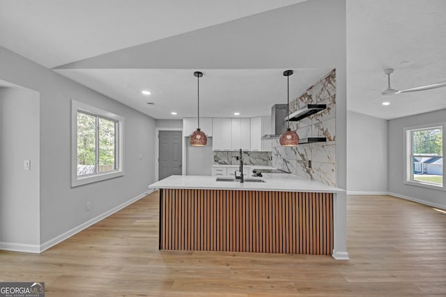 kitchen with backsplash, a sink, light countertops, white cabinets, and a peninsula