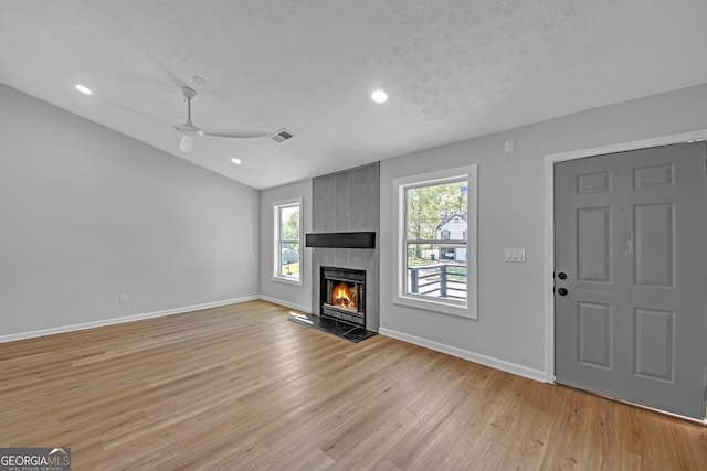 unfurnished living room featuring a ceiling fan, baseboards, light wood-type flooring, lofted ceiling, and a tile fireplace