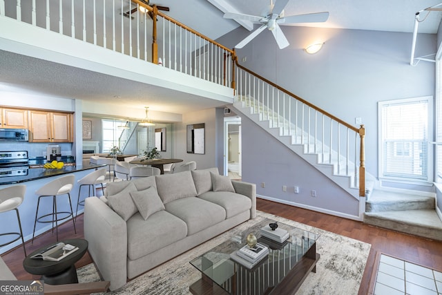 living area featuring stairway, a ceiling fan, dark wood-style flooring, and a towering ceiling