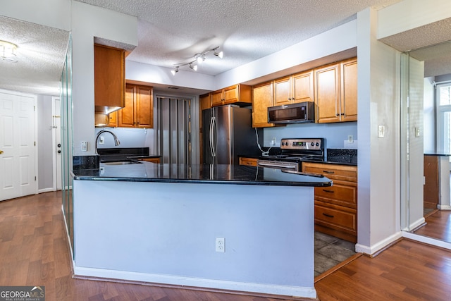 kitchen featuring dark wood-style flooring, dark countertops, a textured ceiling, a sink, and appliances with stainless steel finishes