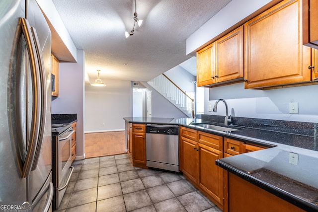 kitchen with appliances with stainless steel finishes, a sink, a textured ceiling, brown cabinetry, and a peninsula
