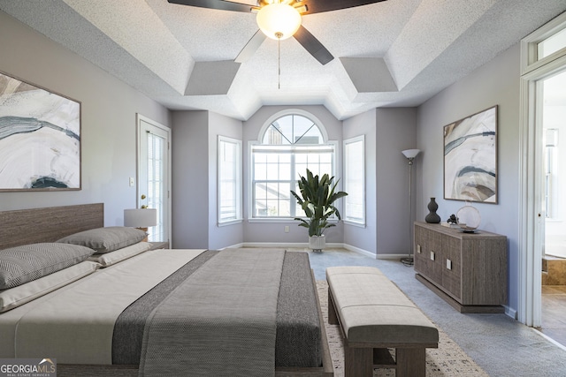 bedroom featuring light carpet, a textured ceiling, a ceiling fan, baseboards, and a tray ceiling