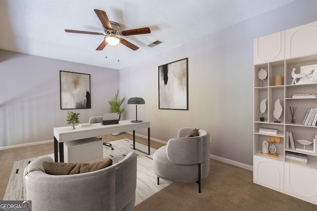 carpeted office featuring visible vents, a textured ceiling, baseboards, and ceiling fan