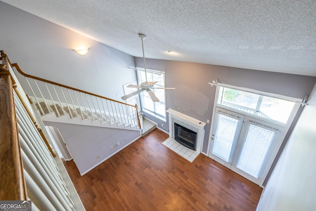 unfurnished living room featuring a textured ceiling, a tiled fireplace, stairs, a ceiling fan, and wood finished floors