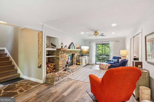 living room featuring stairs, wood finished floors, ceiling fan, and a stone fireplace