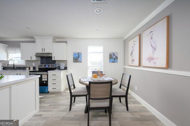 dining area with baseboards, visible vents, ornamental molding, and light wood-style floors