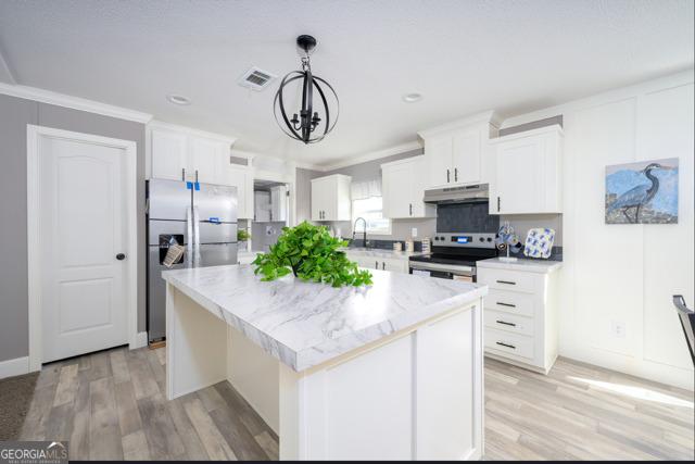 kitchen featuring an inviting chandelier, under cabinet range hood, appliances with stainless steel finishes, white cabinetry, and a center island