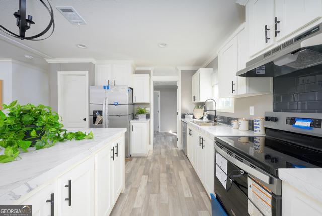 kitchen featuring under cabinet range hood, appliances with stainless steel finishes, ornamental molding, a sink, and visible vents