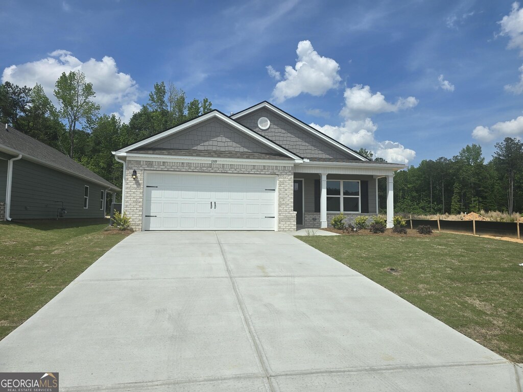 view of front of property featuring an attached garage, concrete driveway, brick siding, and a front yard