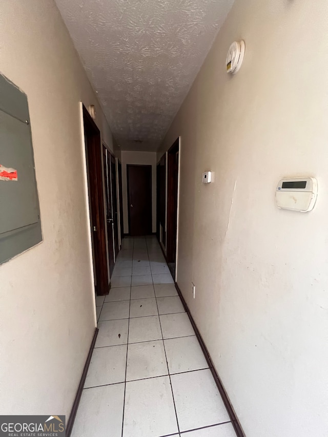 hallway with light tile patterned floors, a textured ceiling, and electric panel