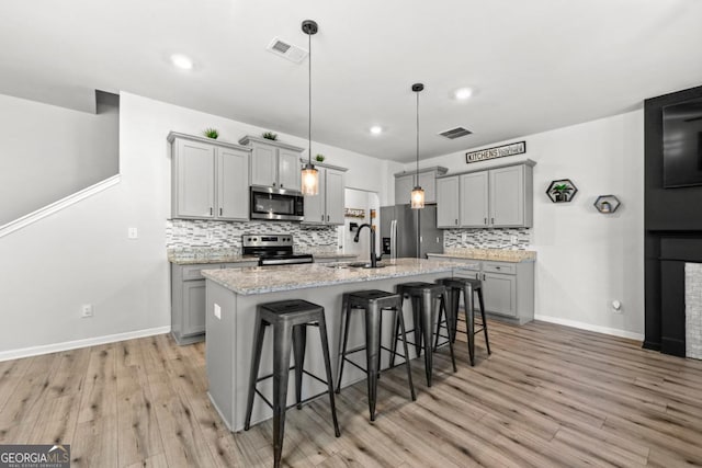 kitchen with gray cabinets, stainless steel appliances, a sink, visible vents, and a kitchen breakfast bar