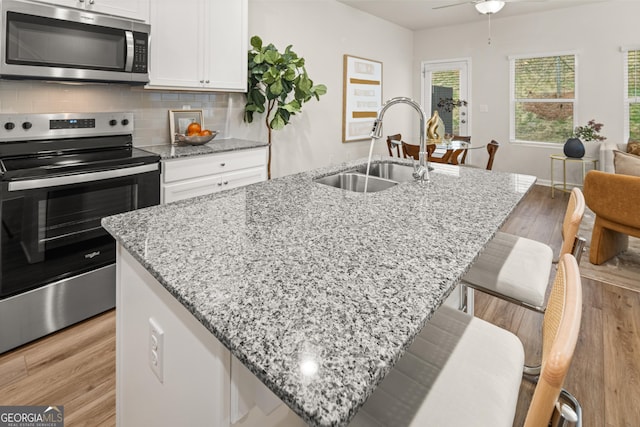 kitchen featuring decorative backsplash, a center island with sink, white cabinets, a sink, and stainless steel appliances
