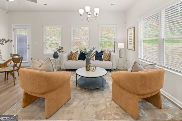 living area featuring light wood-style floors, ceiling fan with notable chandelier, and visible vents