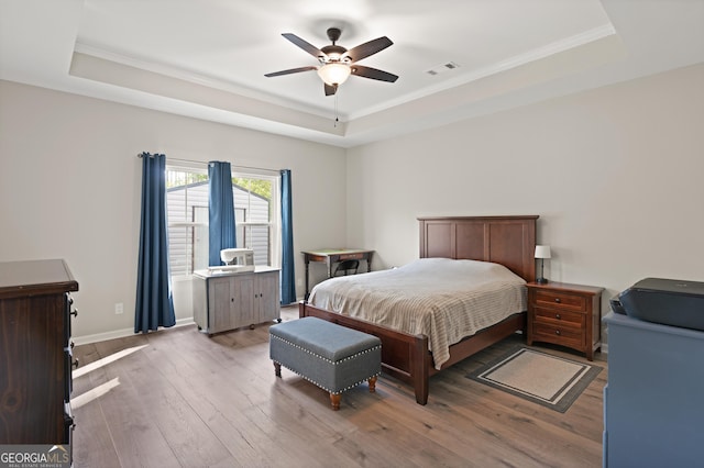 bedroom featuring visible vents, a raised ceiling, light wood-type flooring, and ornamental molding