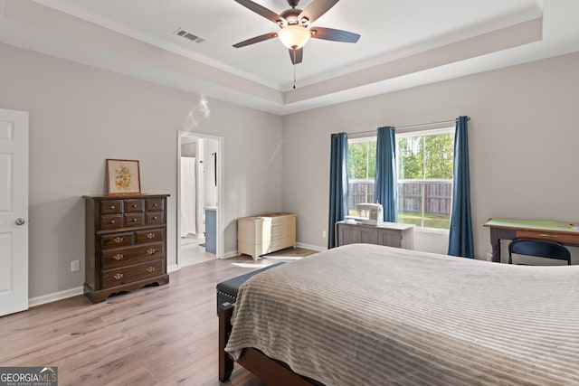 bedroom featuring crown molding, visible vents, a tray ceiling, baseboards, and wood finished floors