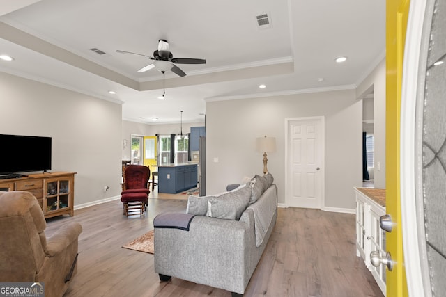 living area featuring ornamental molding, visible vents, and a tray ceiling