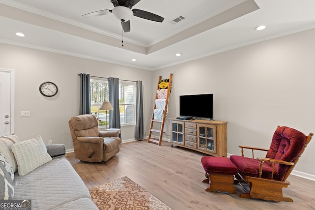living room with a raised ceiling, visible vents, wood finished floors, and a ceiling fan