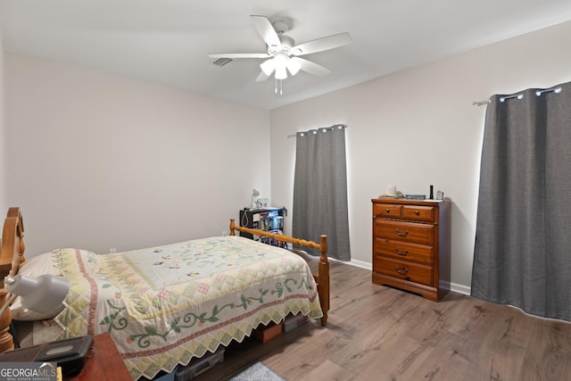 bedroom featuring wood finished floors, a ceiling fan, visible vents, and baseboards