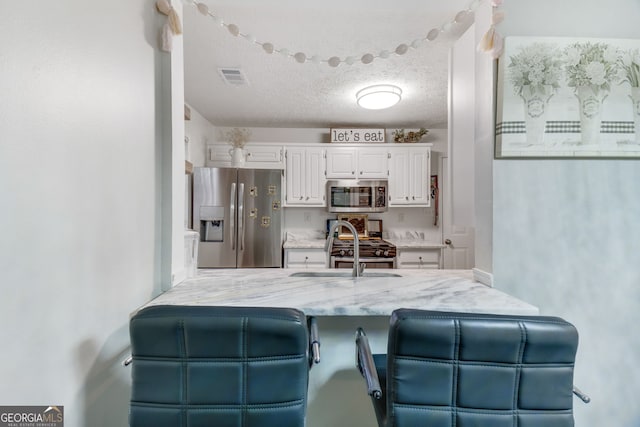 1029 Megan Ct, Sugar Hill, GA 30518 - kitchen with stainless steel appliances, white cabinets, a sink, light stone counters, and a peninsula