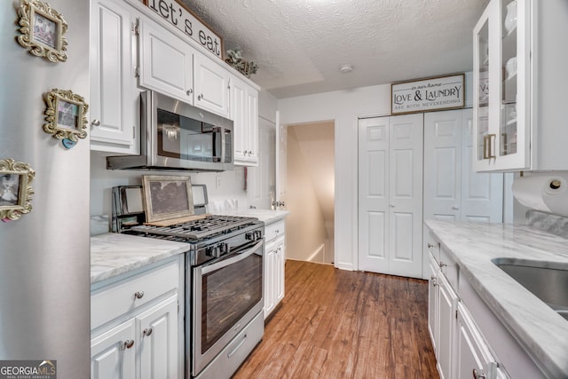 1029 Megan Ct, Sugar Hill, GA 30518 - kitchen with stainless steel appliances, wood finished floors, white cabinets, glass insert cabinets, and light stone counters