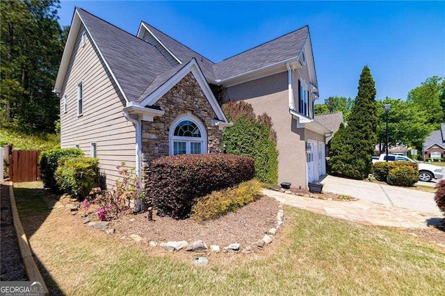 view of front of property featuring fence, a front yard, stone siding, concrete driveway, and an attached garage