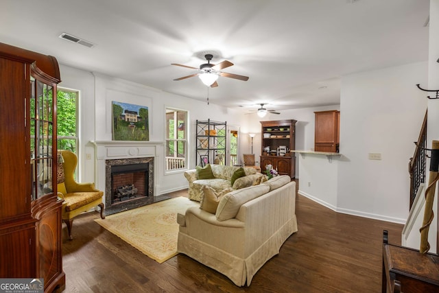 living room featuring dark wood finished floors, visible vents, a ceiling fan, and a premium fireplace