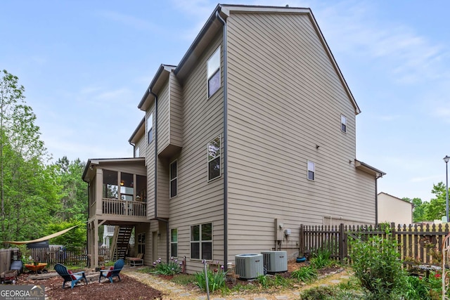 exterior space featuring a fire pit, cooling unit, stairs, fence, and a sunroom