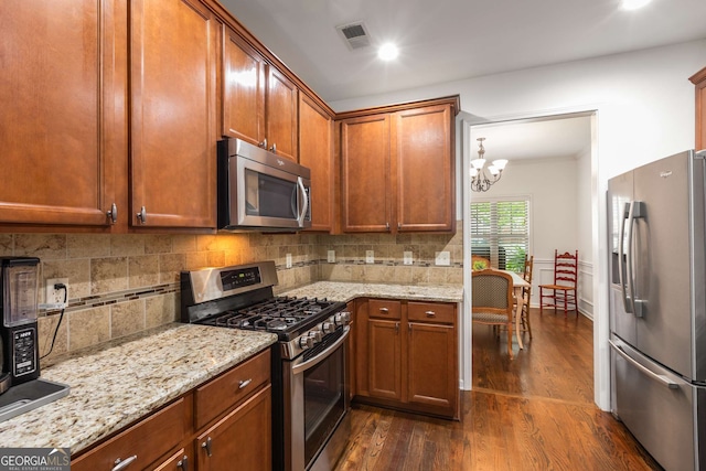 kitchen with a chandelier, appliances with stainless steel finishes, decorative backsplash, and dark wood-type flooring