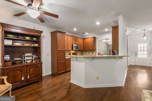 kitchen featuring light stone countertops, brown cabinetry, appliances with stainless steel finishes, dark wood-style floors, and a peninsula