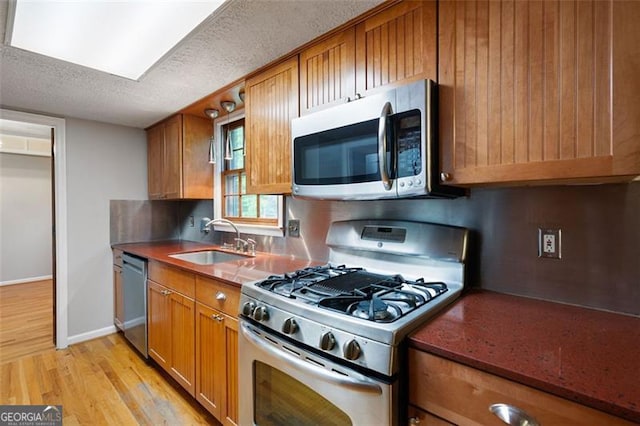 kitchen featuring brown cabinetry, appliances with stainless steel finishes, a sink, light wood-type flooring, and a textured ceiling
