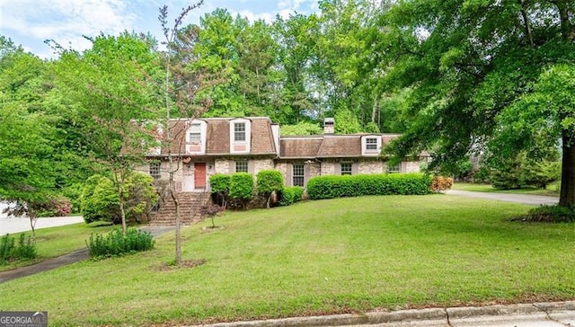 view of front of house featuring a front lawn, a chimney, and mansard roof