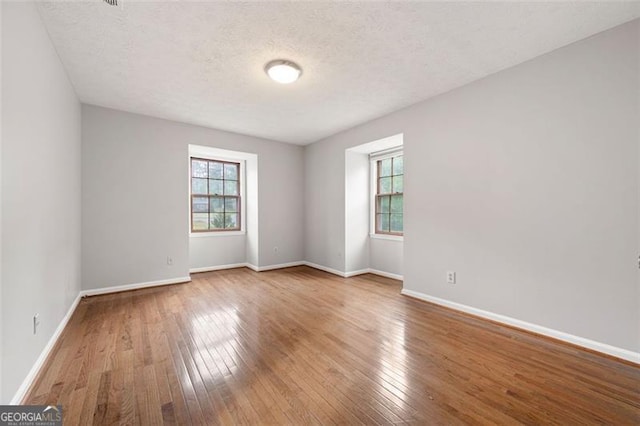 spare room featuring baseboards, hardwood / wood-style flooring, and a textured ceiling