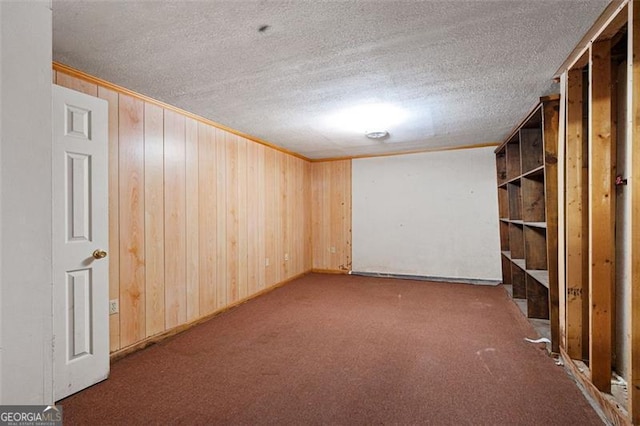 finished below grade area with ornamental molding, wooden walls, a textured ceiling, and carpet flooring