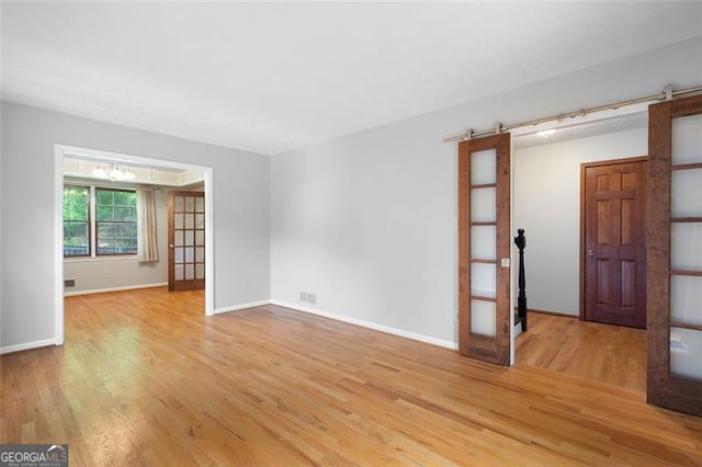empty room featuring a barn door, a notable chandelier, visible vents, light wood-style flooring, and baseboards
