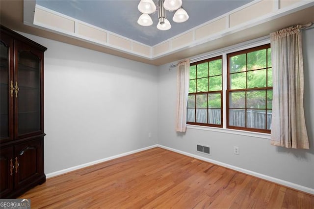 empty room featuring visible vents, a notable chandelier, light wood-style flooring, and baseboards