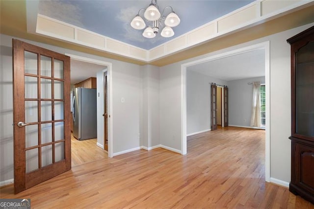 unfurnished room featuring a chandelier, baseboards, and light wood-style floors